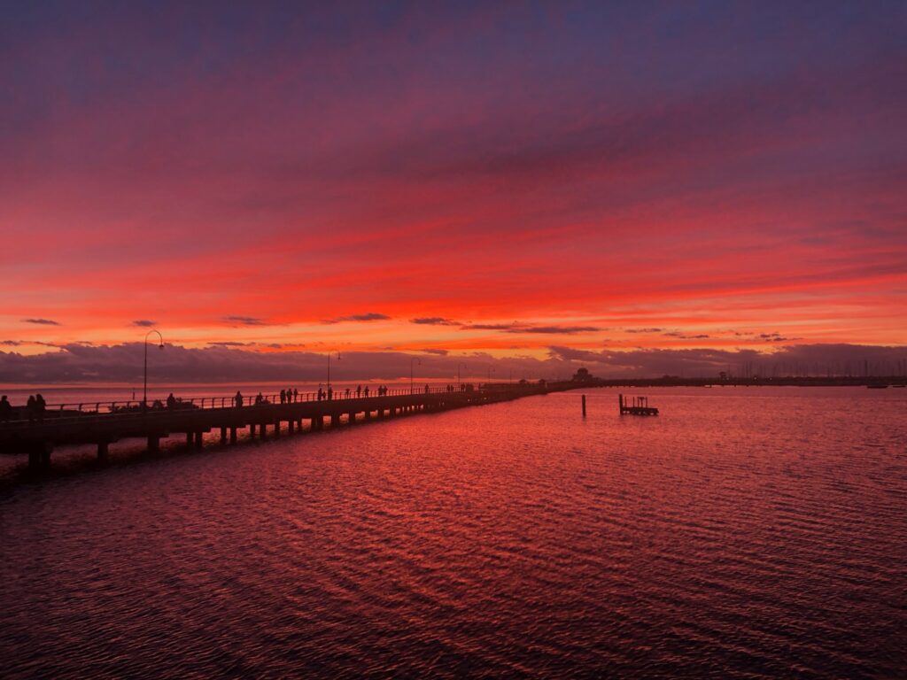 silhouette of st kilda pier over body of water during sunset