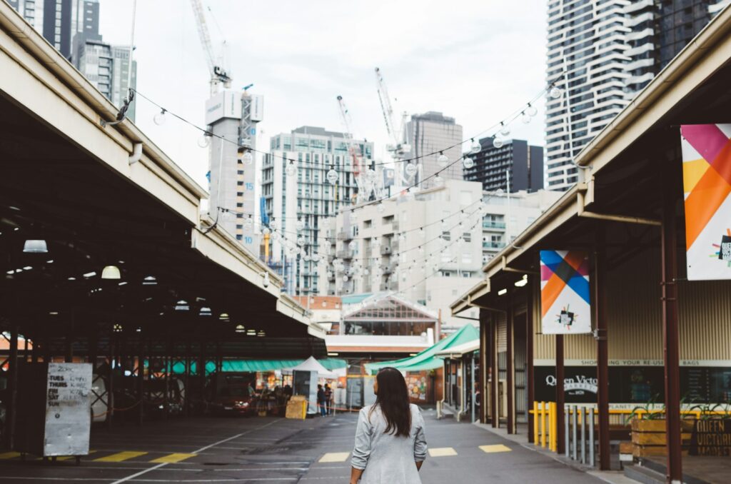 photo of woman standing on roadway between buildings at queen victoria market